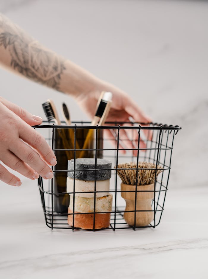 Eco-conscious storage of toiletries in a modern wire basket held by tattooed hands on marble surface.