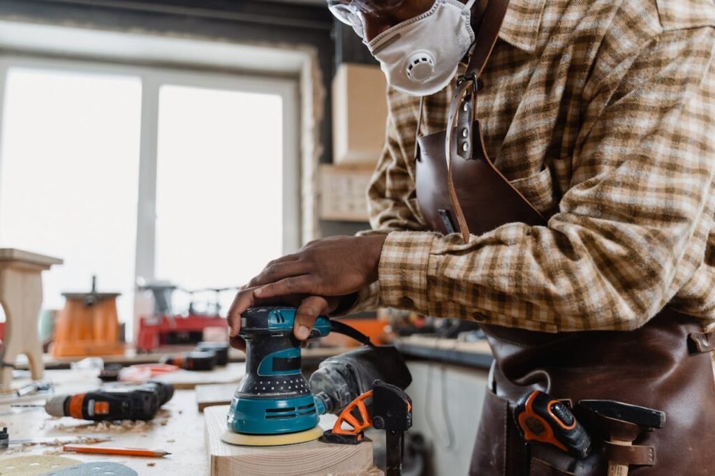 Skilled craftsman using an orbital sander on a wooden board in a workshop.